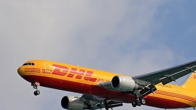 A DHL cargo airplane flying high against a clear blue sky, showcasing logistics and air transport.